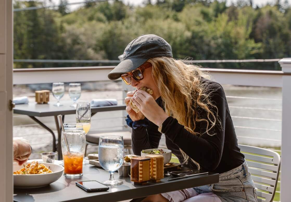 woman with long hair and ball cap biting into food 1118x774 compressed-1